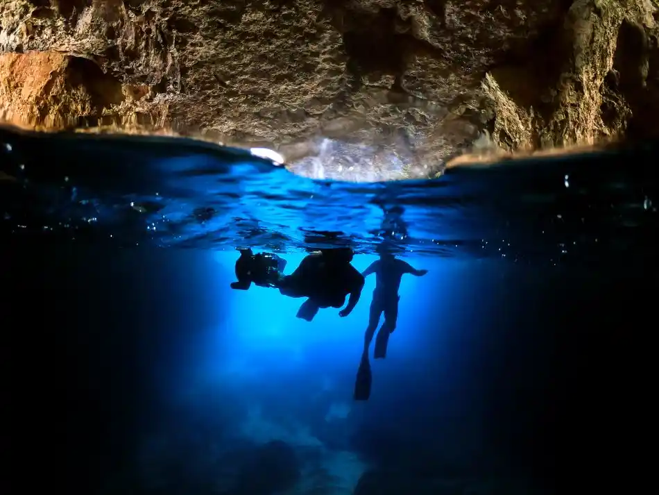 Freediving beneath a rock arch in the clear cyan sea off Malta.