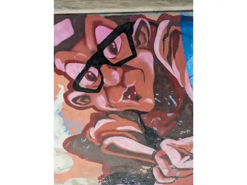 A young man with large glasses,  with a cynical look, Malta Street Art