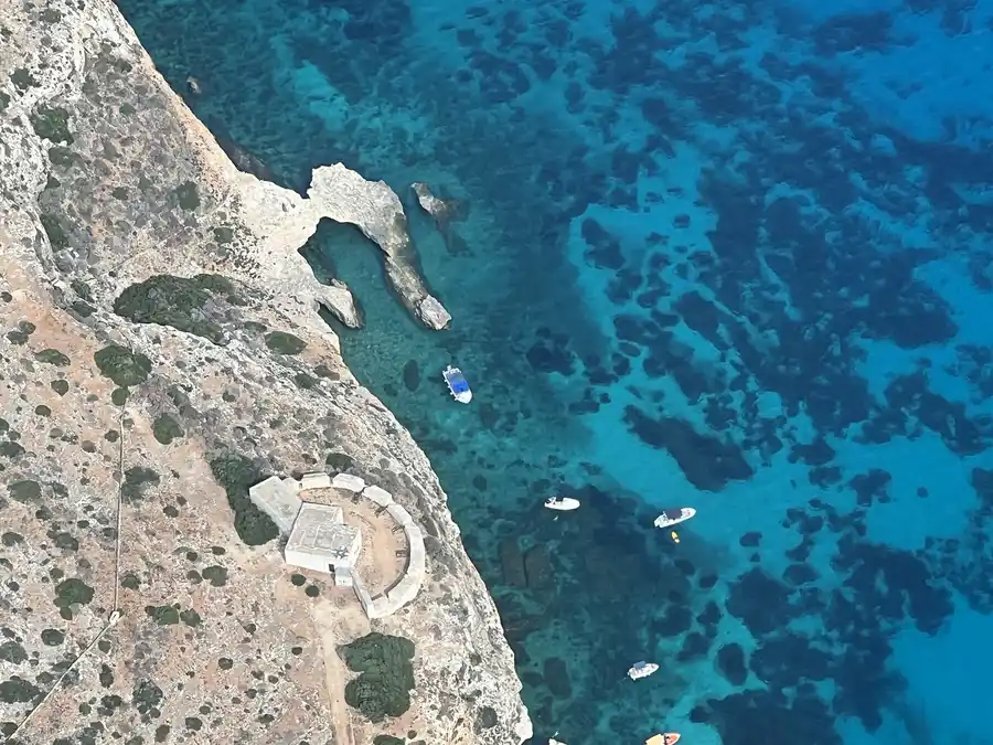 Comino from above, with Santa Maria Tower on the headland and small boats moored in the turquoise water below