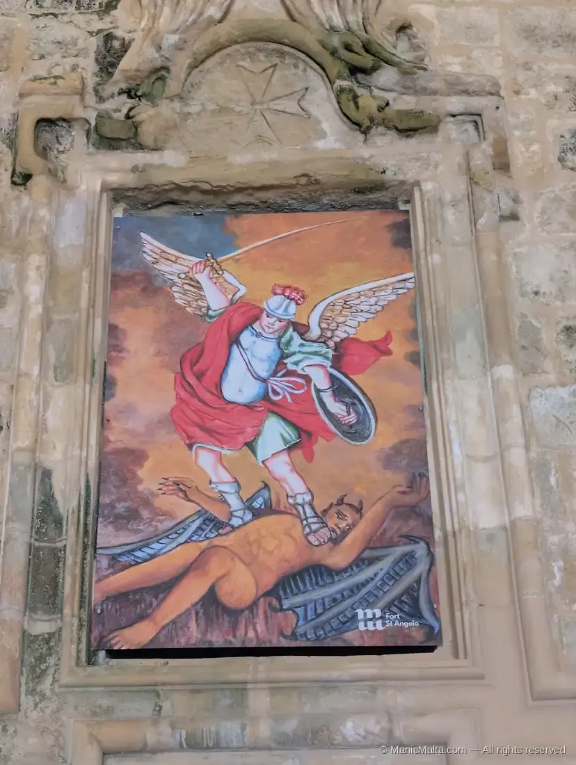A painted panel of the Archangel Michael trampling Lucifer, set into a stone wall above the inner entrance of Fort St Angelo, with a Maltese Cross carved above