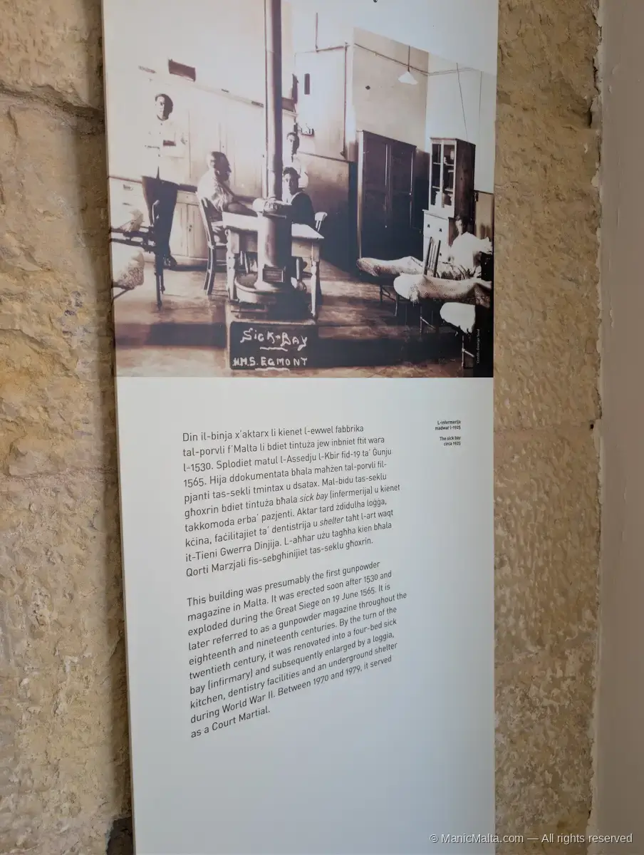 Interior panel at Fort St Angelo with an archival photograph of HMS Egmont's sick bay and bilingual Maltese/English text describing the building's use as gunpowder magazine, naval infirmary, WWII shelter and court martial venue