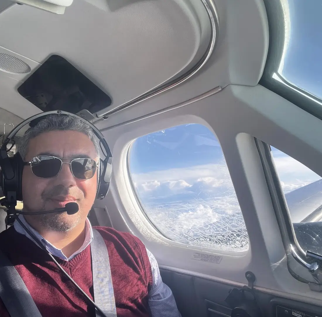 View from inside a small aircraft over Malta, with a Malta Wings pilot wearing a headset and clouds visible through the side window