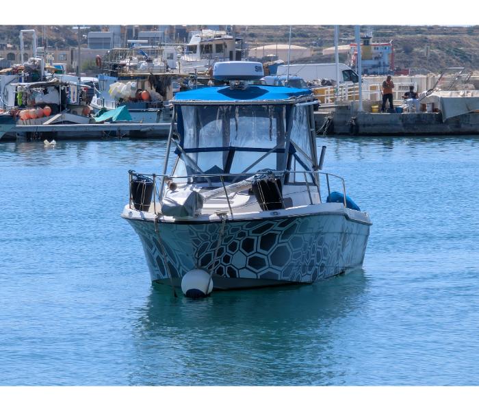 Modern cabin boat with a grey hexagonal camouflage pattern on the hull moored in Marsaxlokk harbour with other fishing boats and the waterfront in the background