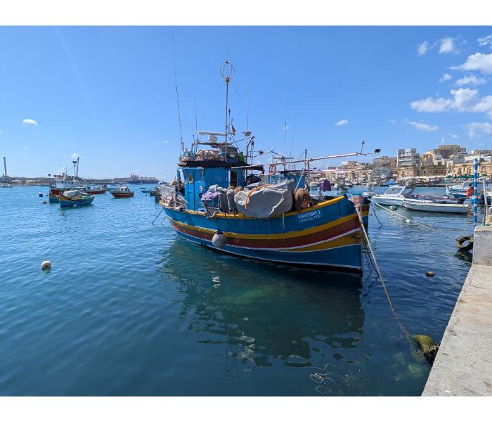 Blue and yellow luzzu Kristofer J registered in Valletta, moored alongside the Marsaxlokk waterfront