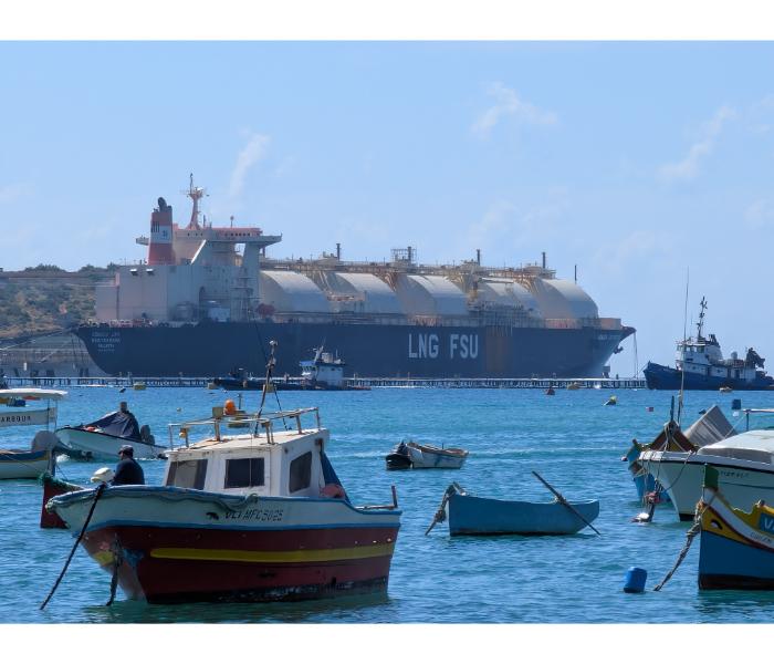 Traditional Maltese luzzu fishing boats moored in Marsaxlokk harbour with the LNG FSU floating storage tanker filling the horizon behind them