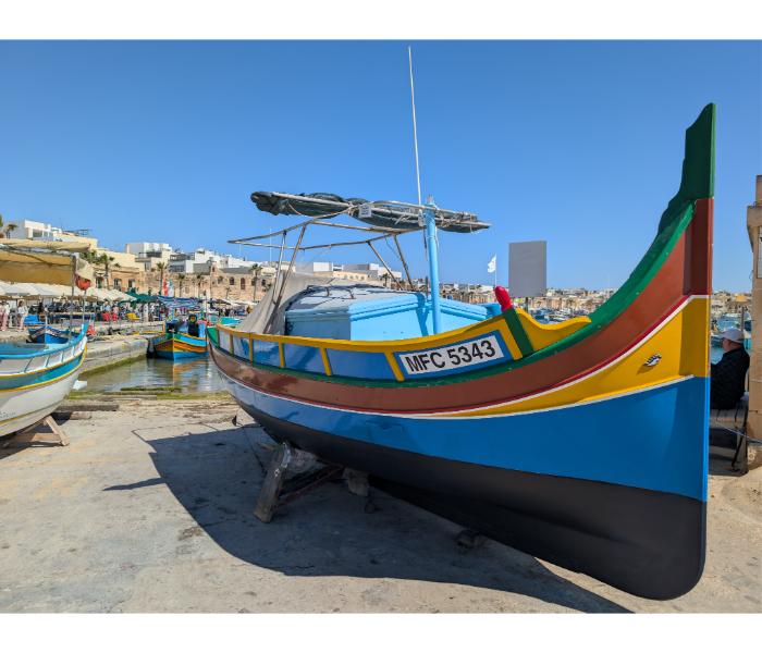 Freshly restored blue luzzu numbered MFC 5343 on stands ashore in Marsaxlokk, with traditional yellow, red, and green trim and a new black waterline