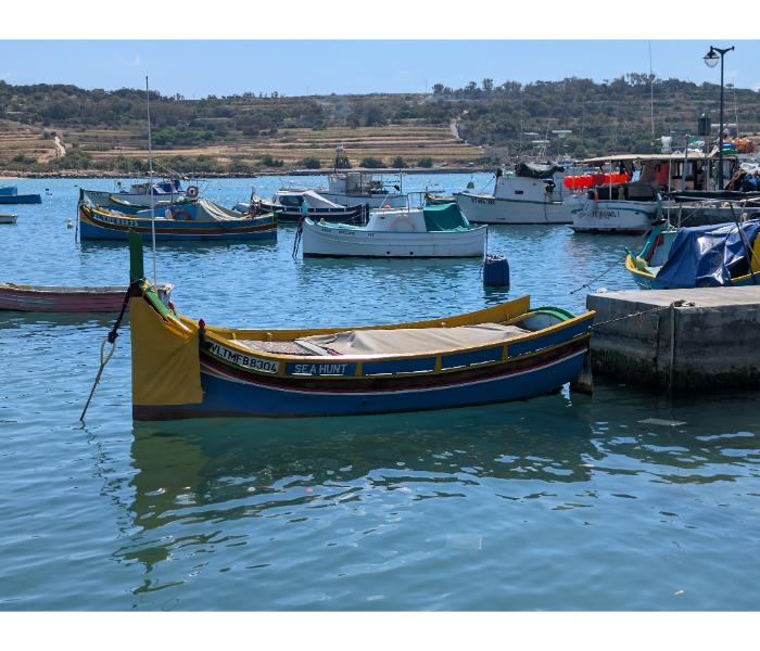 The luzzu Sea Hunt from Valletta moored close to the Marsaxlokk quay with other fishing boats and a low hillside behind
