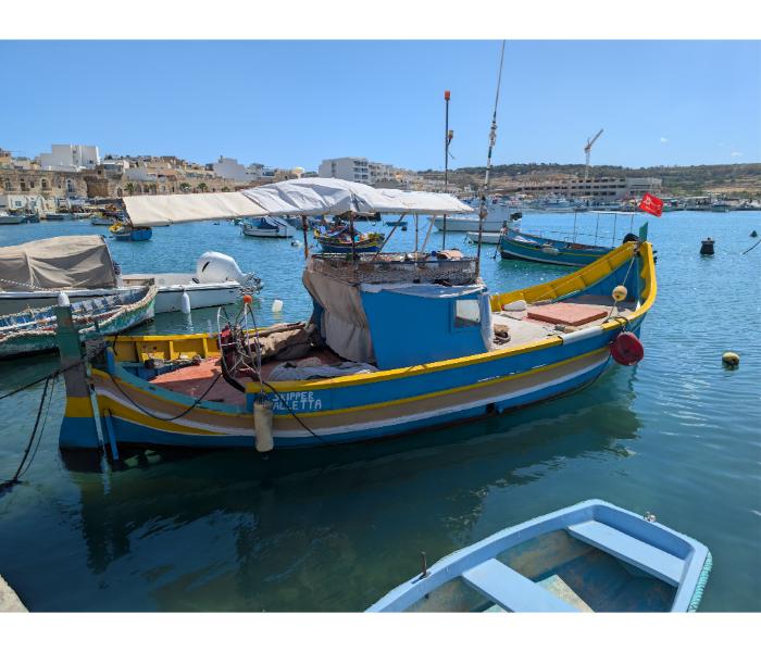 The luzzu Skipper from Valletta with a fitted sun awning over the cockpit, moored in Marsaxlokk harbour