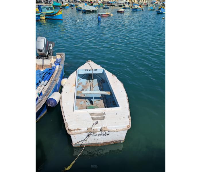 White tender numbered T/T MFC 636 with a small outboard engine moored alongside its larger parent fishing boat in Marsaxlokk