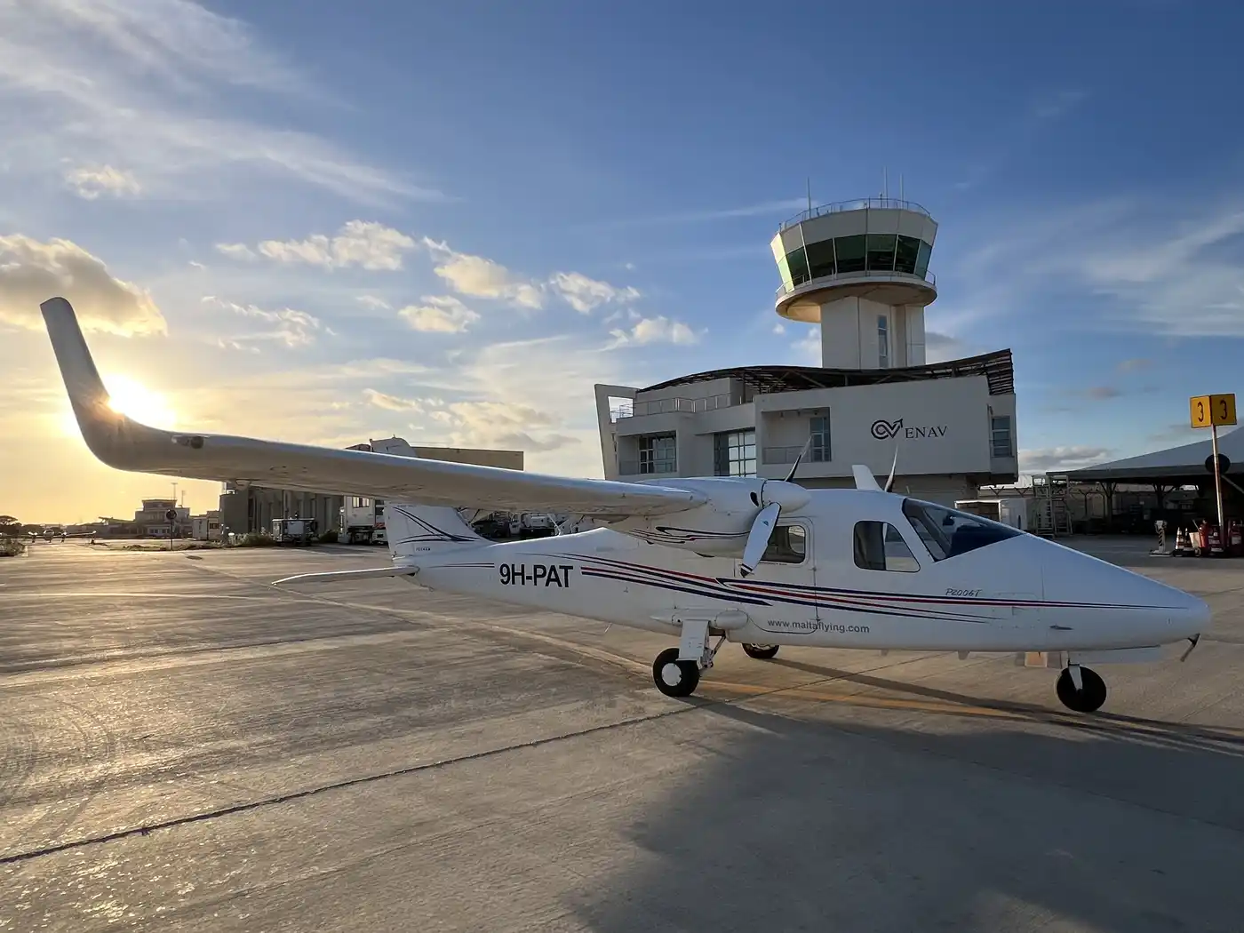 Malta Wings Tecnam P2006T twin-engine aircraft on the apron at sunset, with a control tower behind it
